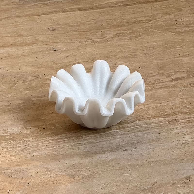 White fluted marble fruit bowl on a light brown marble surface.